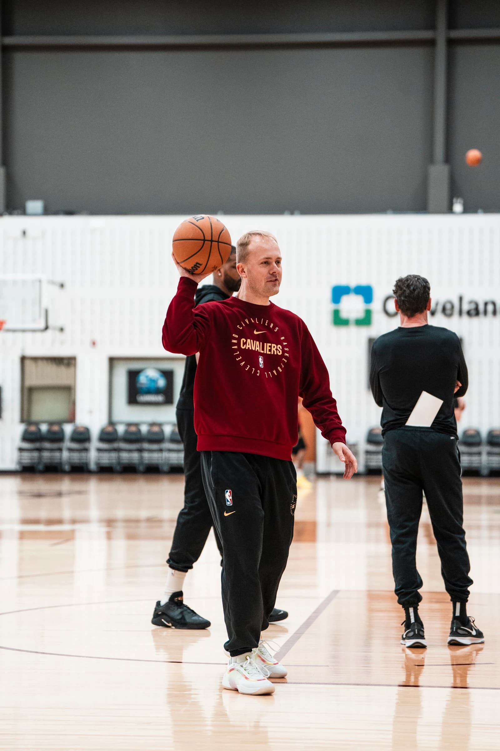 Alex Sarama holding a basketball on the Cavaliers practice court in a burgundy Cavaliers sweatshirt.